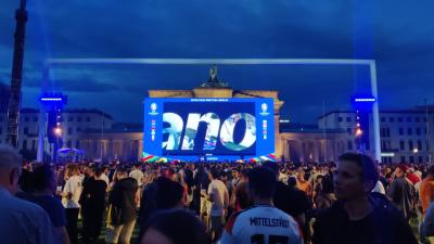 Eine Menschenmenge steht vor dem Brandenburger Tor, vor dem eine Leinwand angebracht ist.